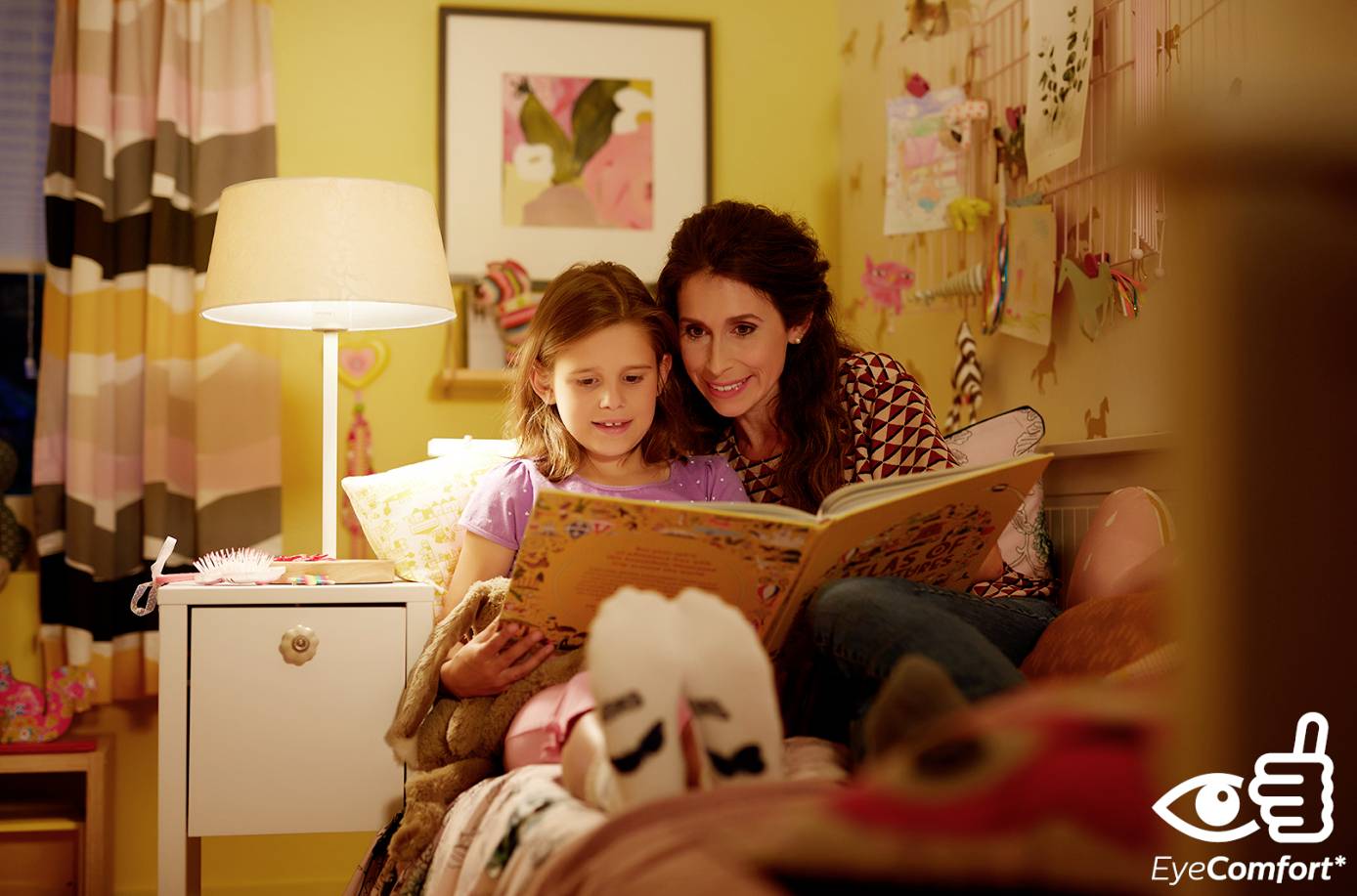 A mother is reading a book with her daughter in the children's bedroom. It's evening, and the warm lighting creates a cosy atmosphere.