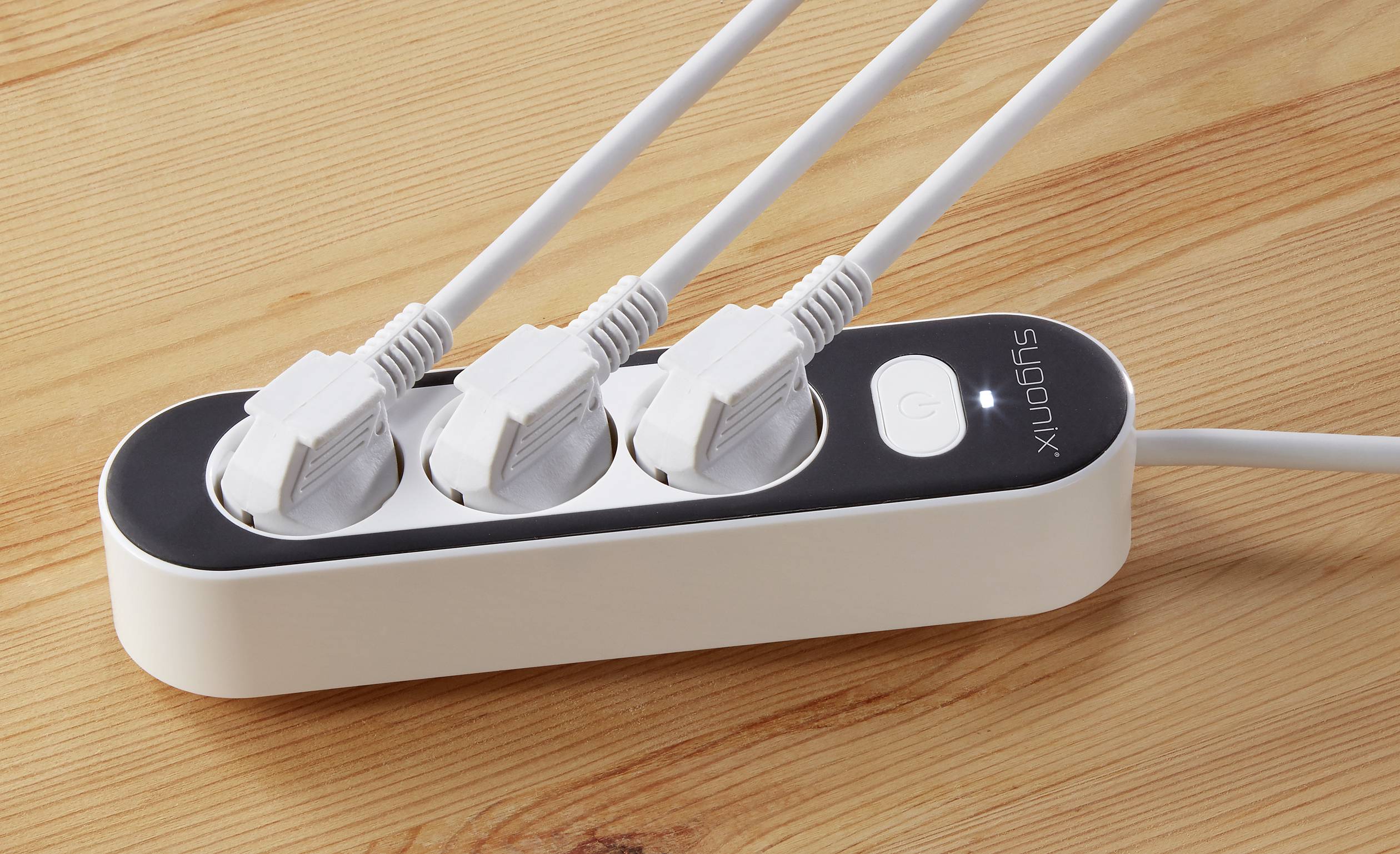 A white multi-socket adaptor with three connected cables on a wooden table.