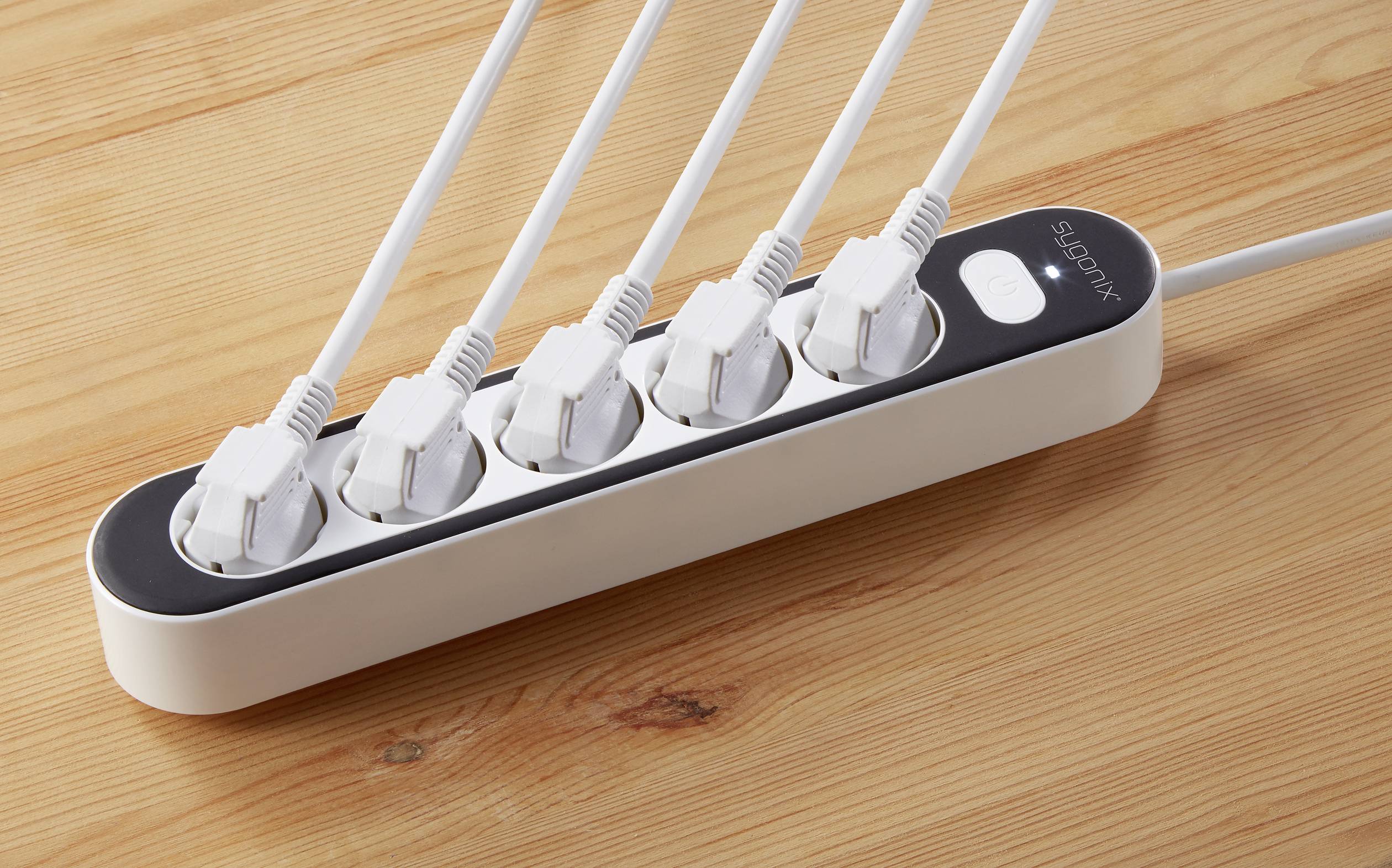 A six-way power strip with six connected white plug adapters on a wooden table.