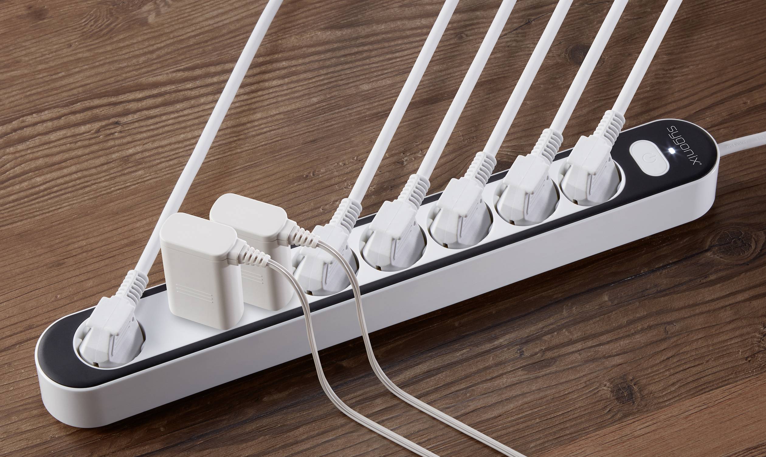 A power strip on a wooden floor is connected to several white cables and two large power adapters.
