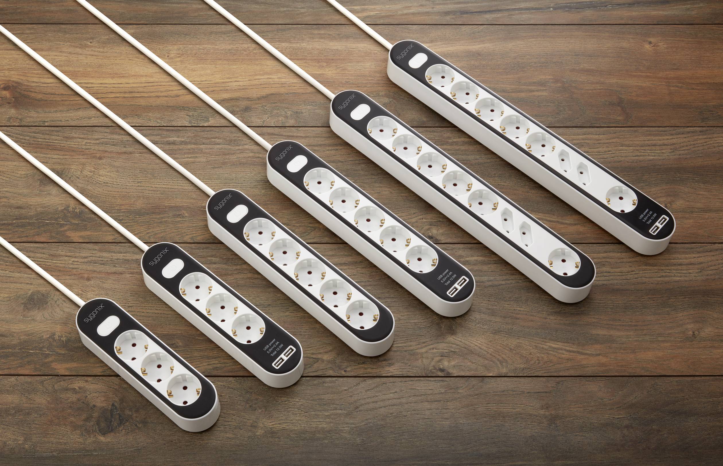 Six multi-socket extension leads with varying numbers of plug sockets arranged on a wooden table.