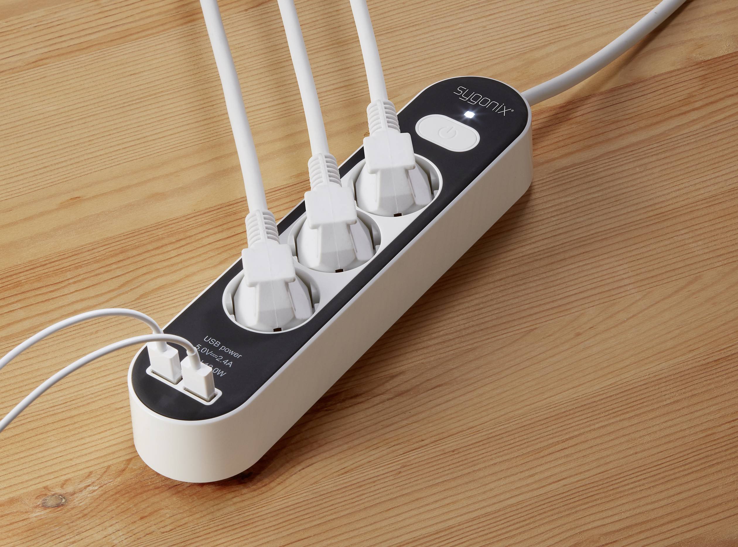 Three white plugs are inserted into a white power strip on a wooden table.