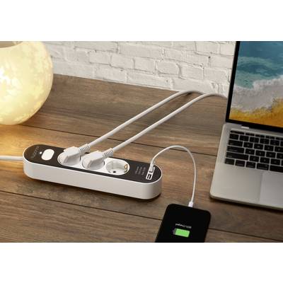 A power strip on a wooden table supplies a laptop and a smartphone with electricity. The smartphone displays a charging process.