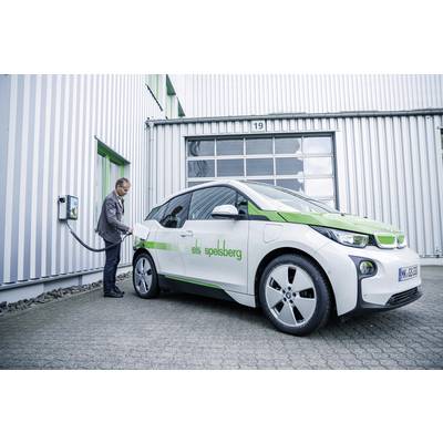 A man is charging an electric car in front of a building. The car is white with green stripes and bears the inscription 'elektro speisberg'.