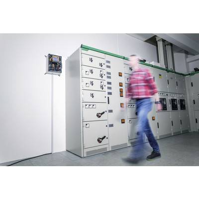 A person in motion in front of a circuit room with switchboards on the wall. The focus is on the technical equipment.