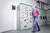 A blurry man in a blouse walks past a control cabinet in a technical room. Cabled devices are located in the background.