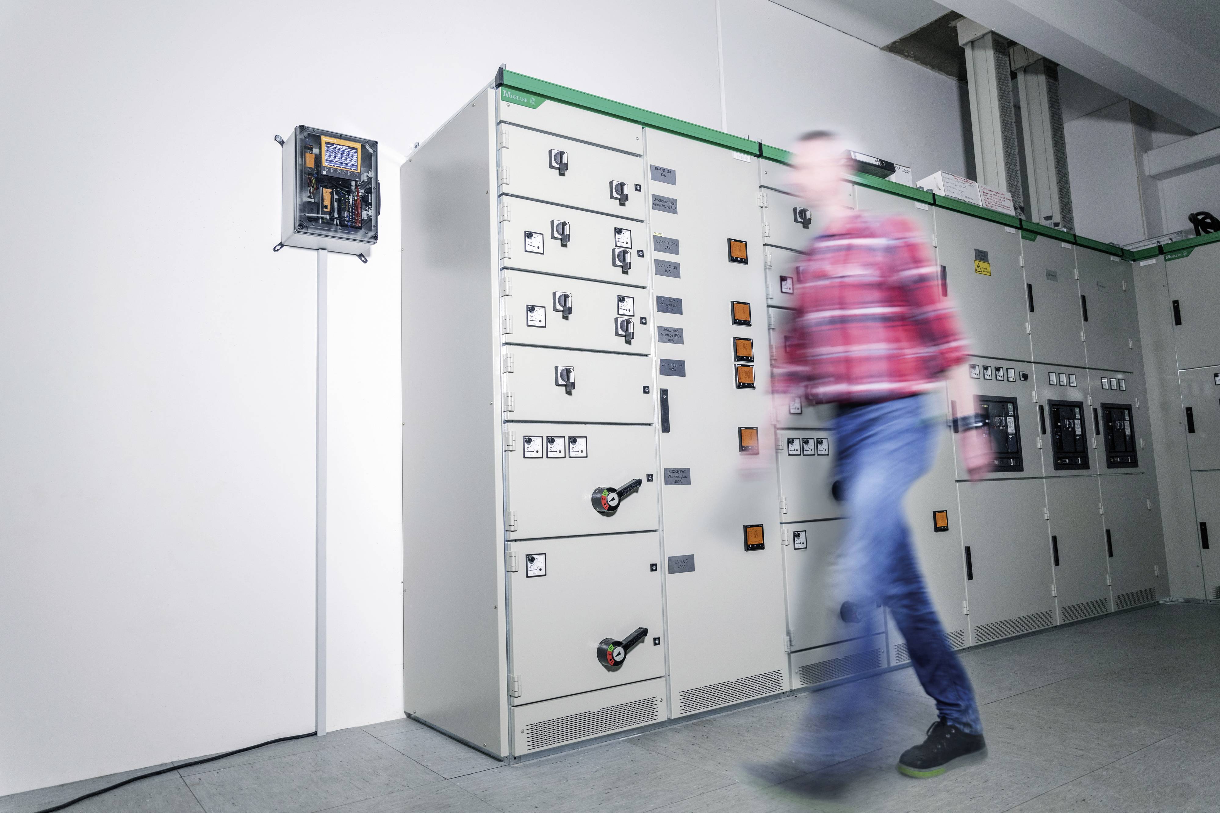 A man in motion in front of a row of large electrical cabinets in a technical room.