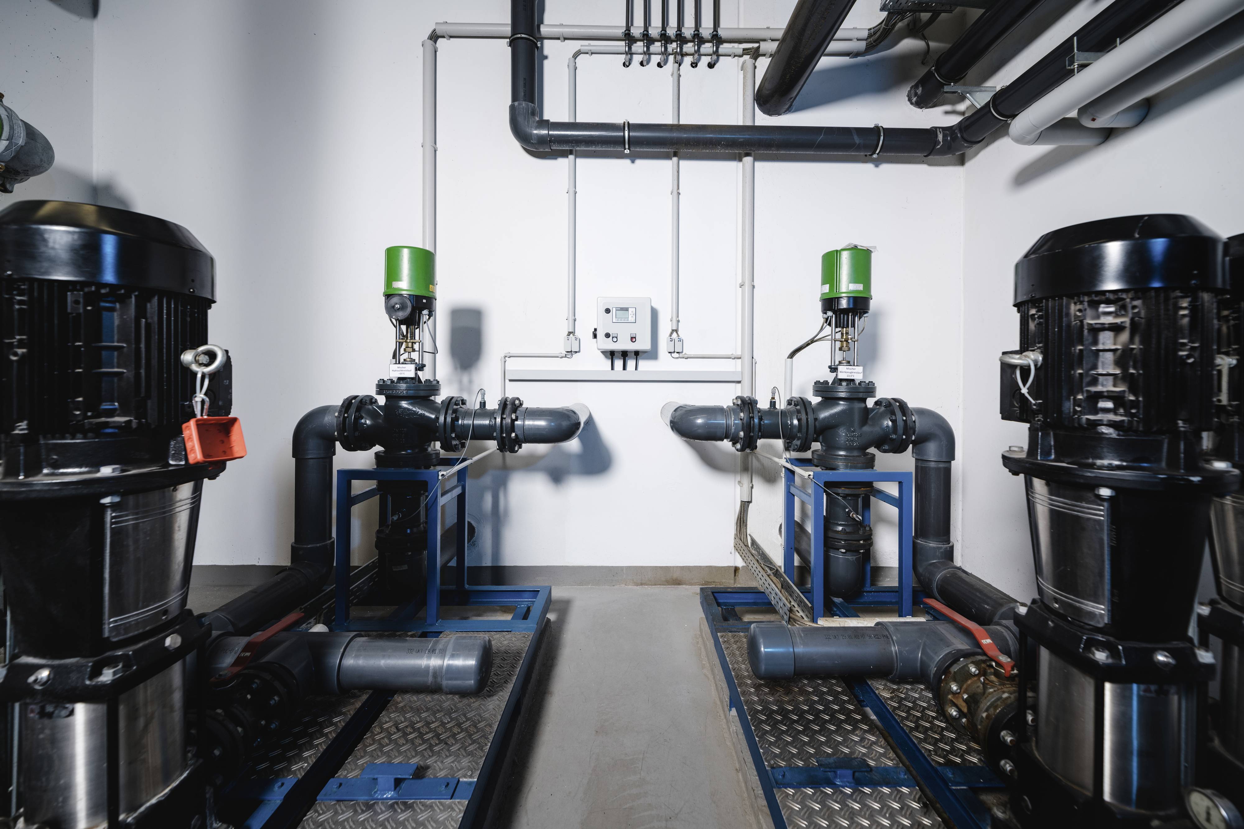 Two industrial pump systems in a technical room. They are symmetrically arranged and connected with pipes and valves.