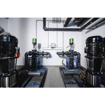 Two industrial pump systems in a technical room. They are symmetrically arranged and connected with pipes and valves.