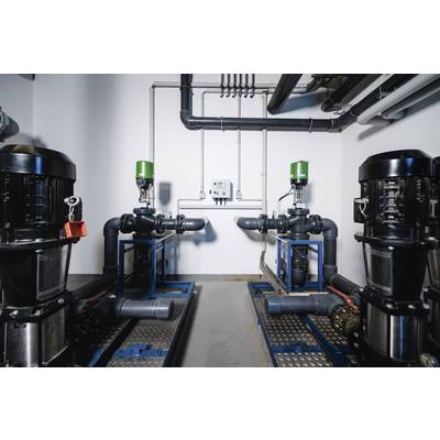 Two industrial pumps in a plant room, connected by pipework, with green-marked valves and a control unit mounted on the wall.