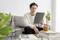 A person is sitting on a sofa and reading on a tablet. A table with books, a mug, and plants is in the foreground.