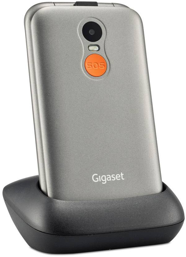 A silver mobile phone by Gigaset sits in a charging station. An orange SOS button is located on the back of the device.