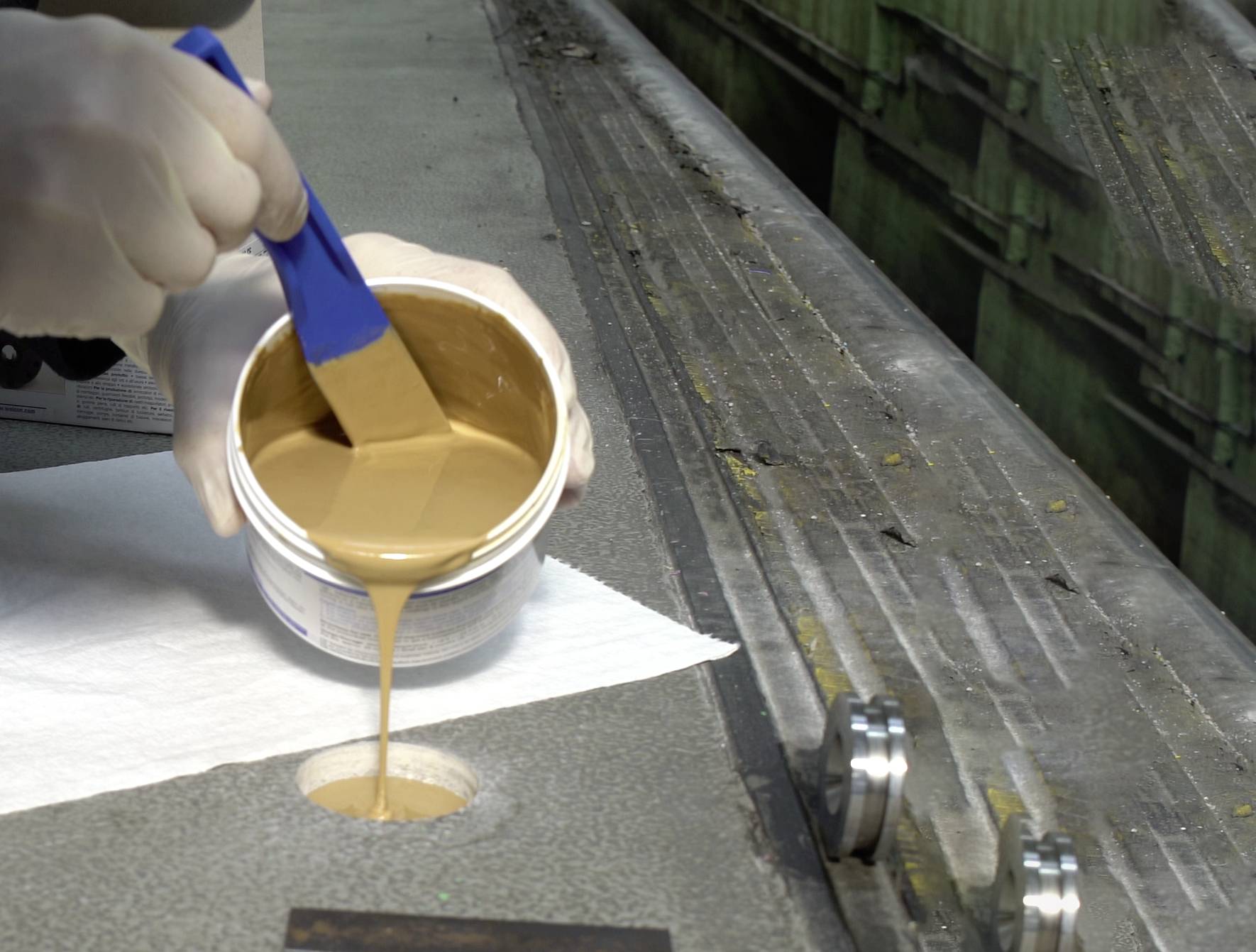 A person is applying a light brown liquid from a container onto a surface using a brush.
