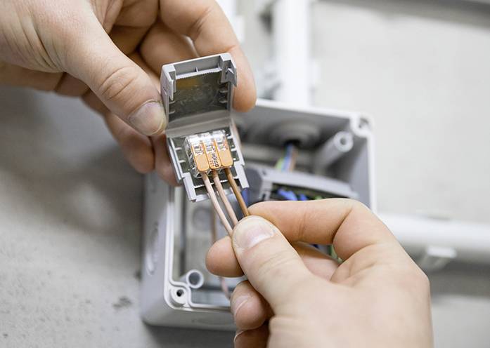 'Hands connect copper wires in an electrical junction box.'