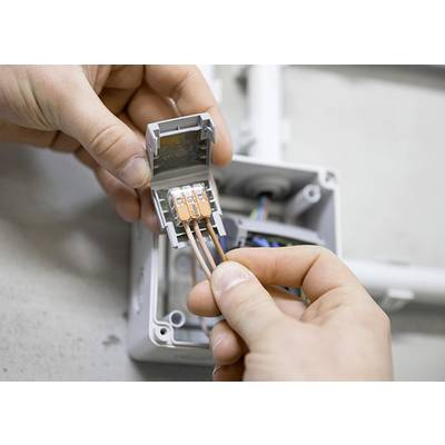 'Hands connect copper wires in an electrical junction box.'