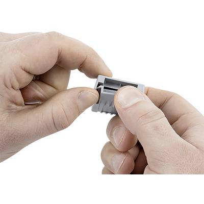 Hands are holding a grey, rectangular plastic plug. One hand is inserting the plug, while the other holds it steady.