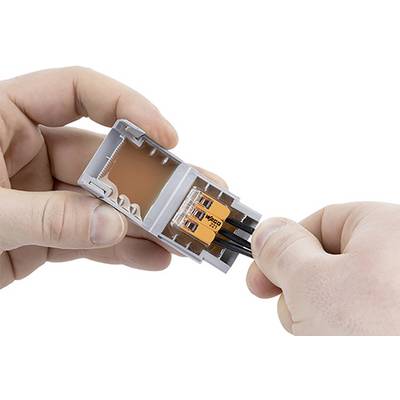 A person connects wires in a grey WAGO terminal block. The left hand holds the block open, while the right hand inserts wires.