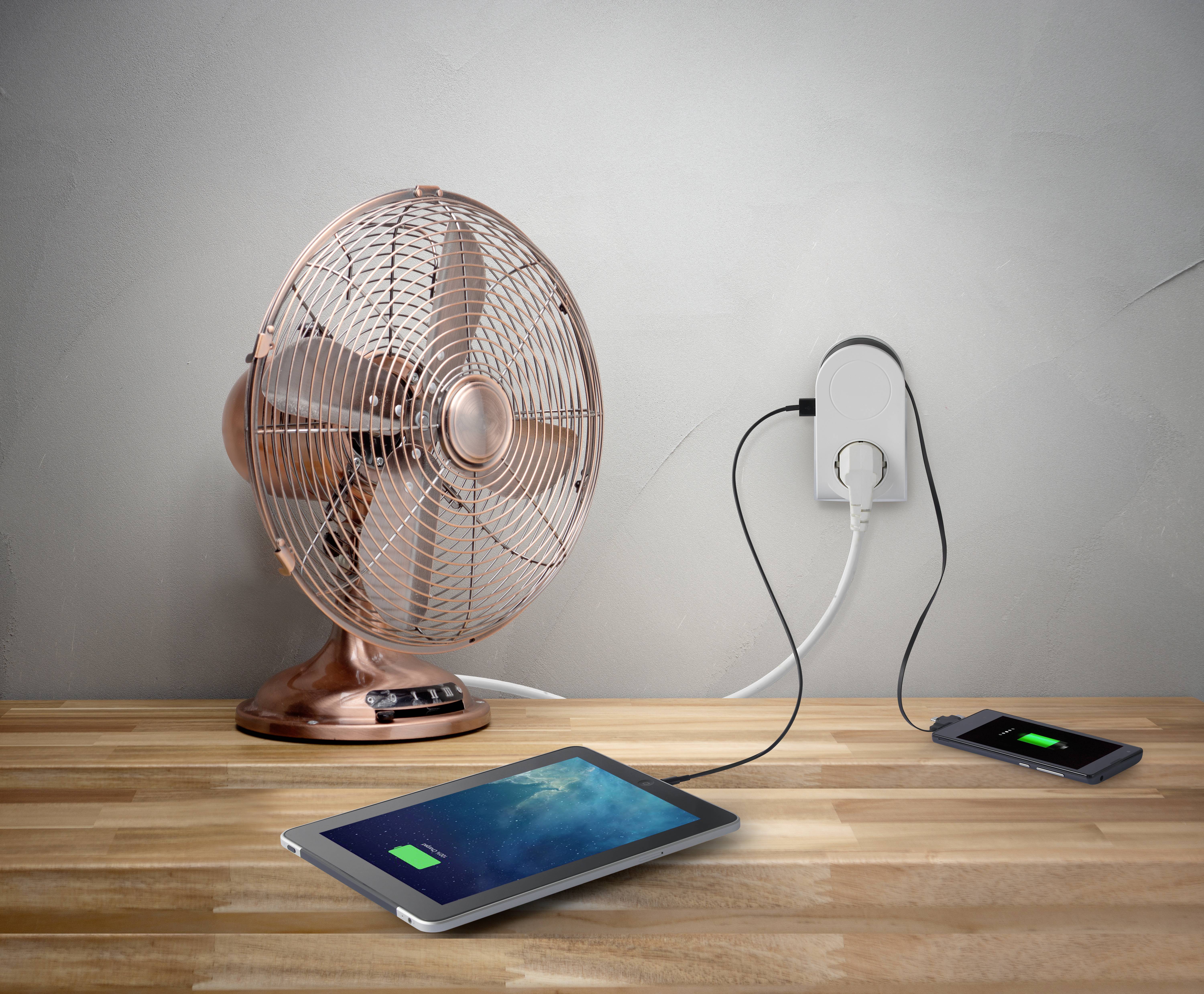 A tablet and a smartphone are lying on a wooden table and charging at a power socket, next to a copper-coloured fan.