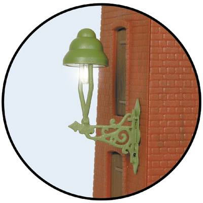 A green lantern is attached to a red brick wall and is illuminating.