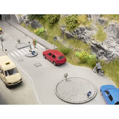 Model street with miniature cars, pedestrian crossing, red car and cyclist on a cycle path along a rocky embankment.