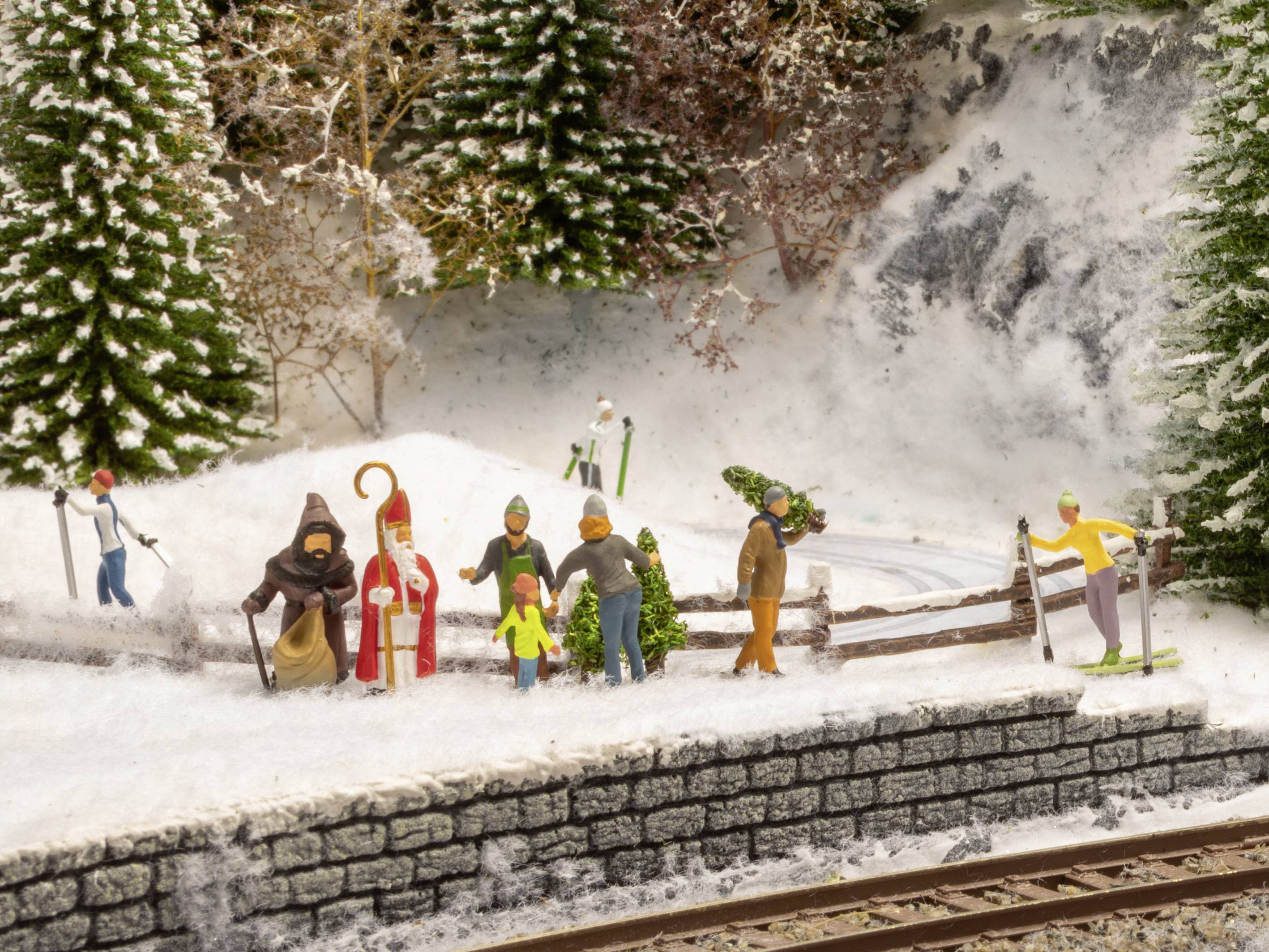 A miniature scene depicts people in winter clothing. Some figures are walking, while others are sledging. Snow-covered trees are in the background.