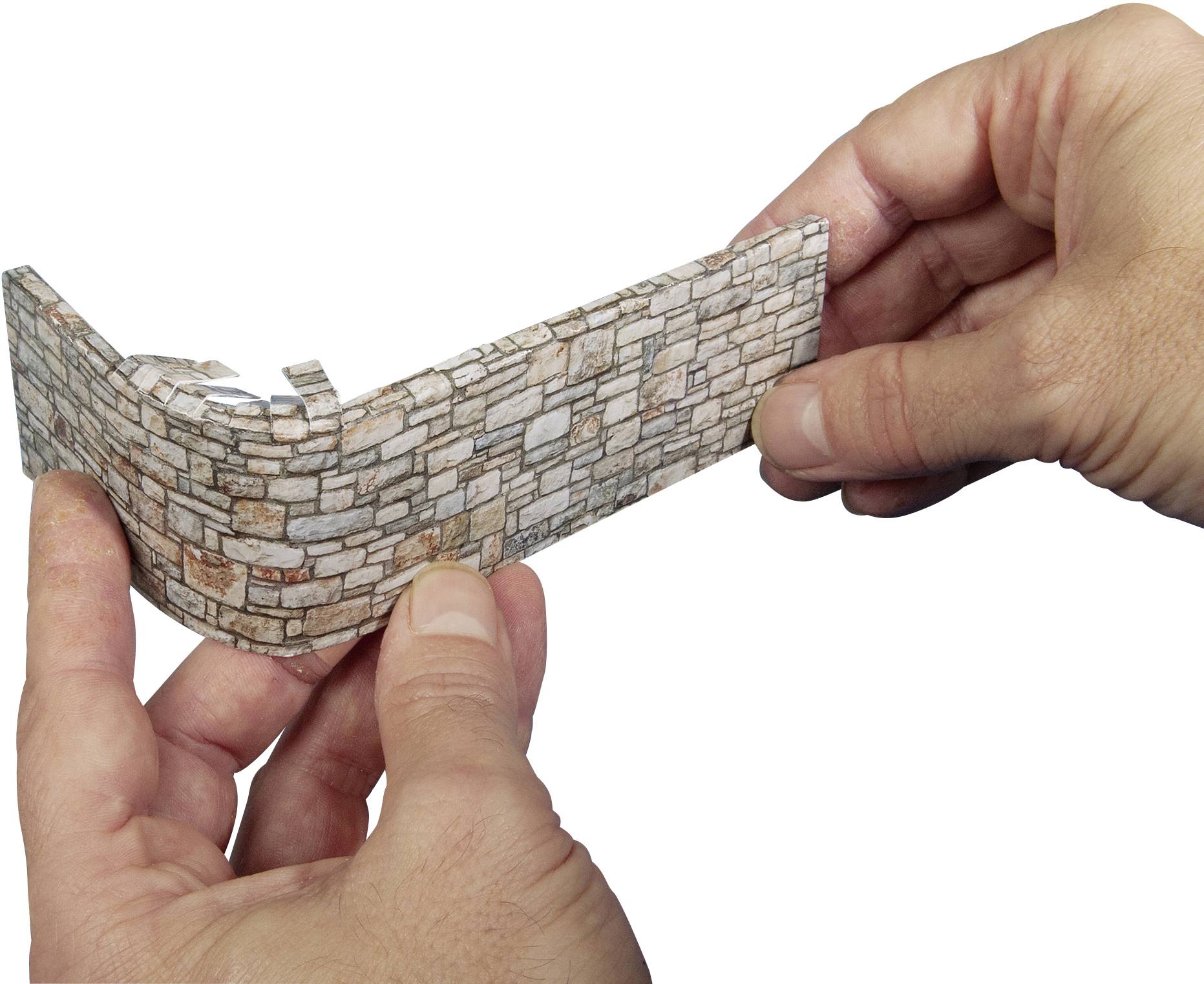 Two hands are holding a small model of a brick wall. The wall is curved and made of light-coloured, rectangular bricks.