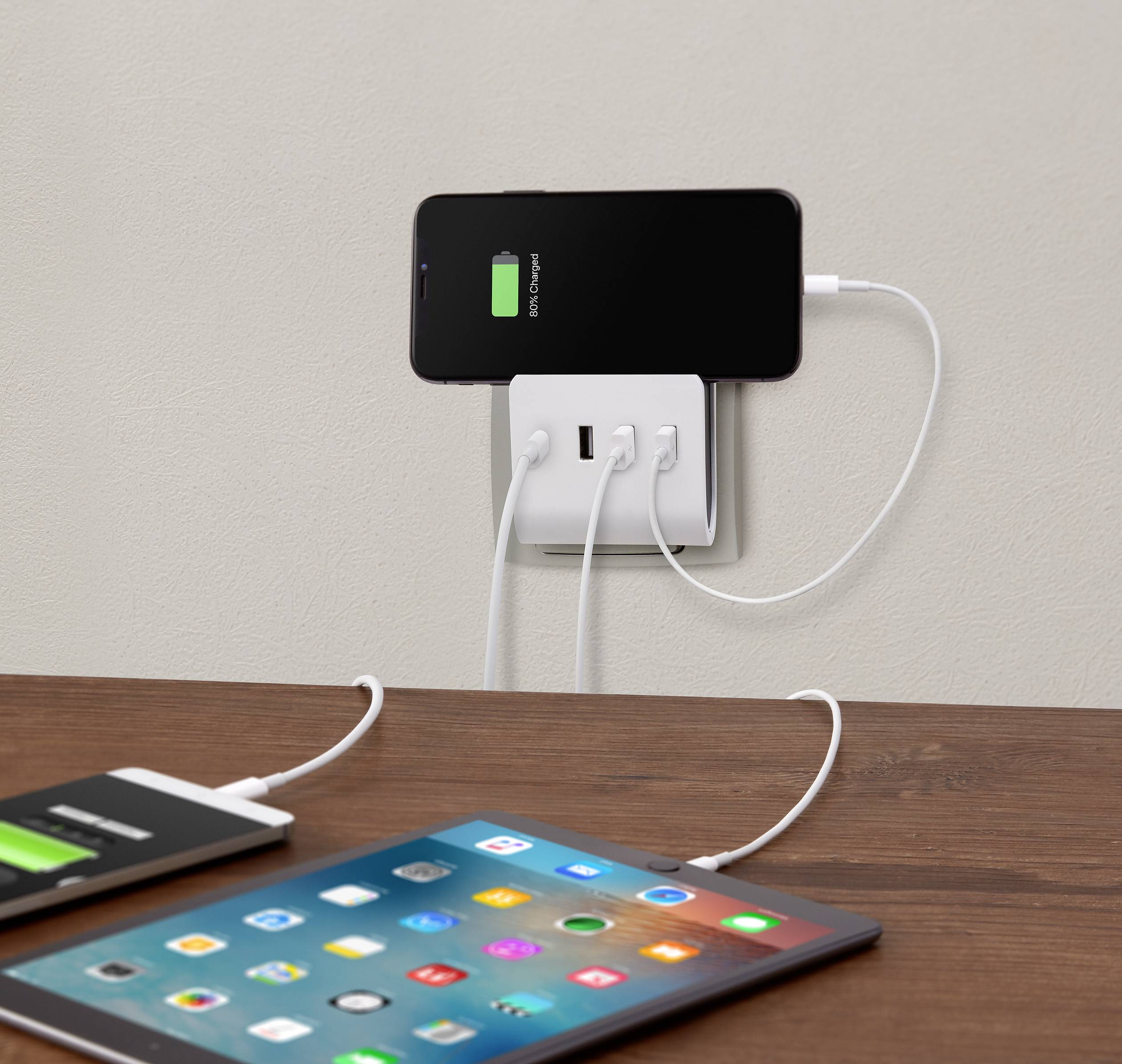 A smartphone and a tablet are being charged via USB cables. The smartphone displays a green charging indicator, showing that it is charging.