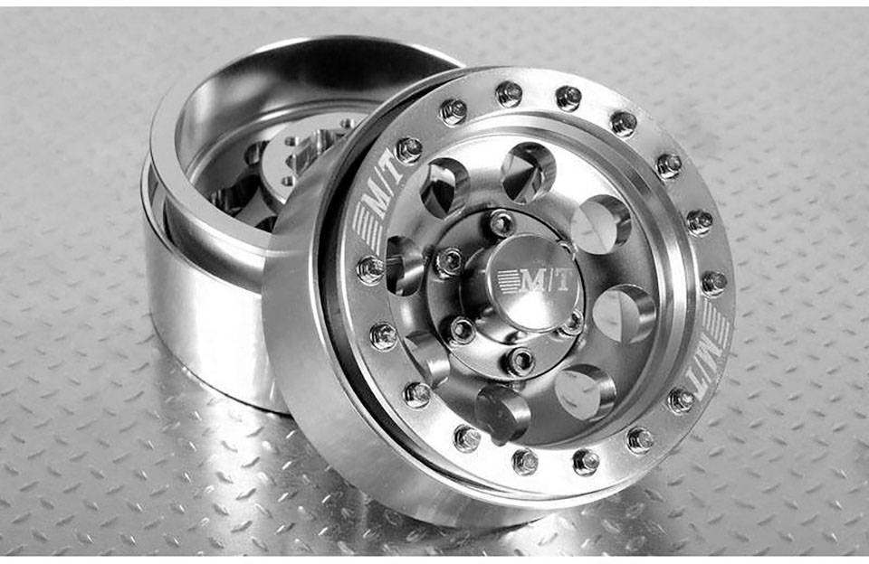 Two gleaming alloy wheels with multiple bolt fixings and an engraved 'M/T' logo, resting on a structured metal background.