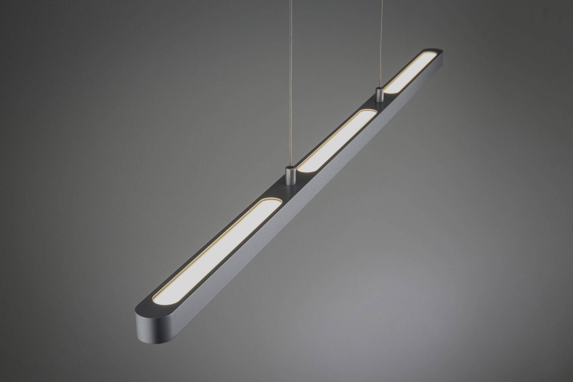 A contemporary, suspended LED light with an elongated, slim design and three illuminating elements in a dark room.