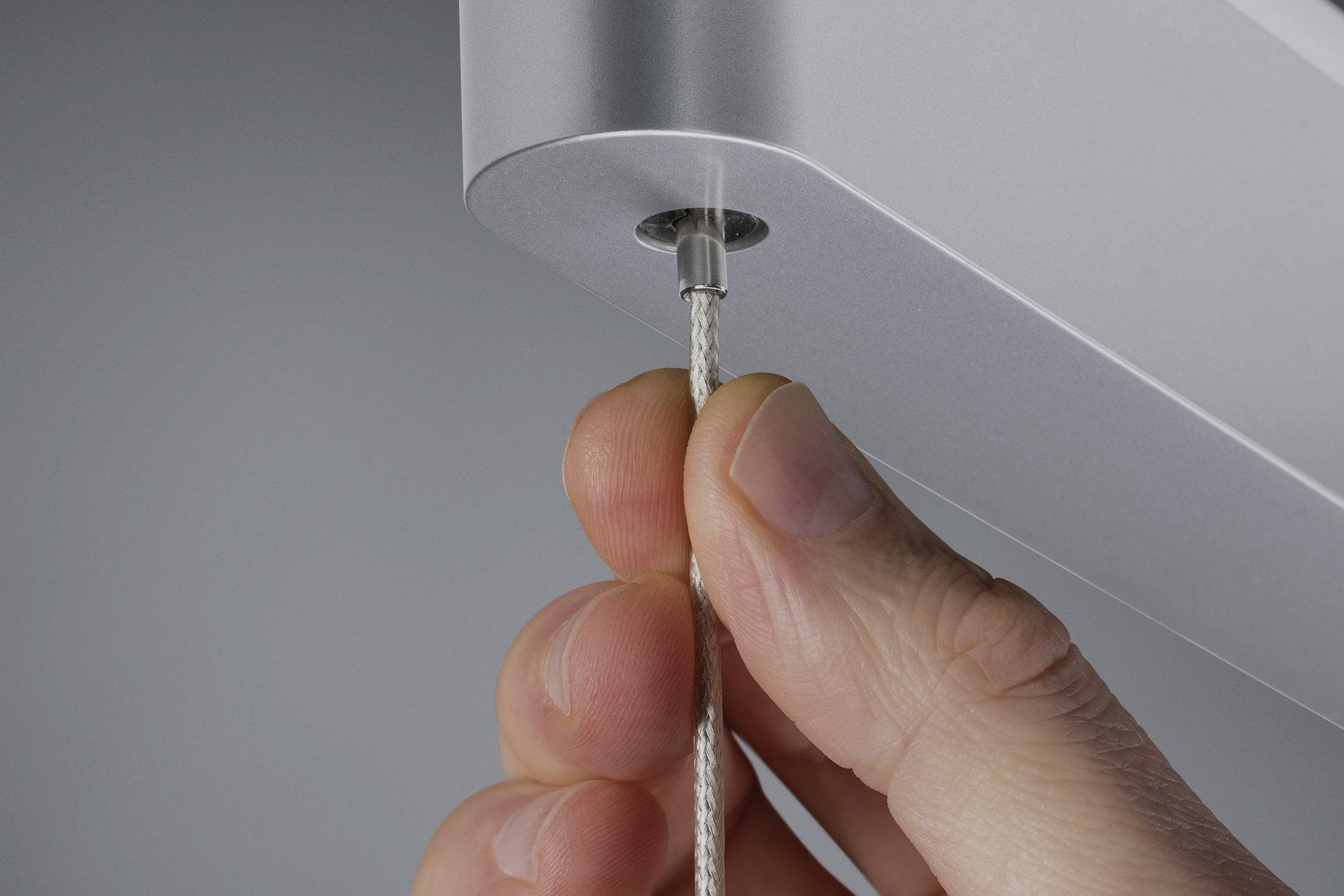 Close-up of a hand inserting a thin cable into a silver device.