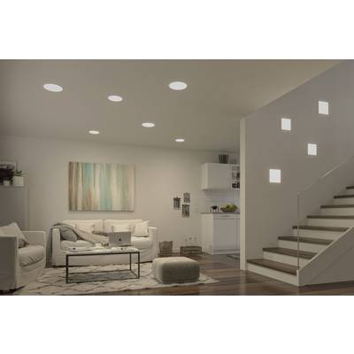 A living room with modern furnishings: sofa, coffee table, laptop, artwork on the wall, open-plan kitchen in the background, illuminated ceiling.