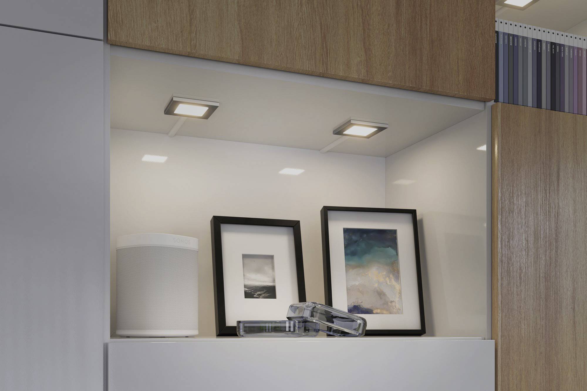 Decorative shelving with contemporary ceiling spotlights. Two framed artworks and a white speaker are displayed.
