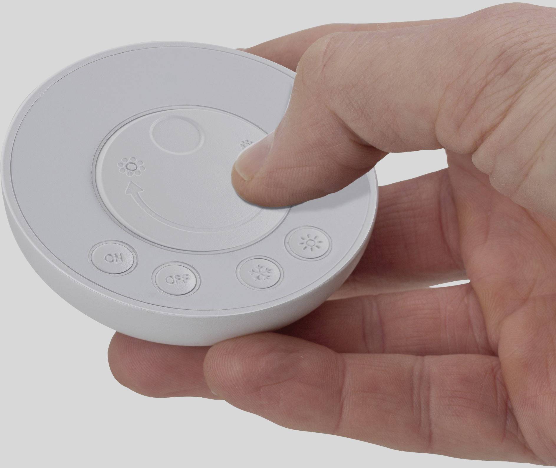 A hand is holding a round remote control with buttons for brightness and on/off. The thumb is pressing a button.