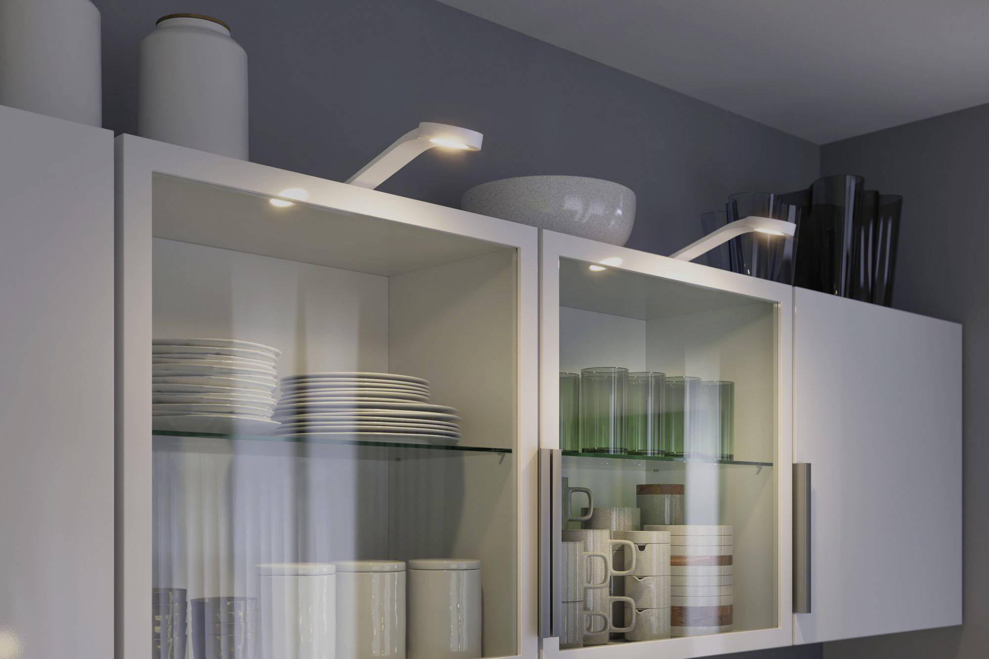 A kitchen cupboard with glass doors displays stacked plates, glasses, and mugs. Two LED lights are mounted above.