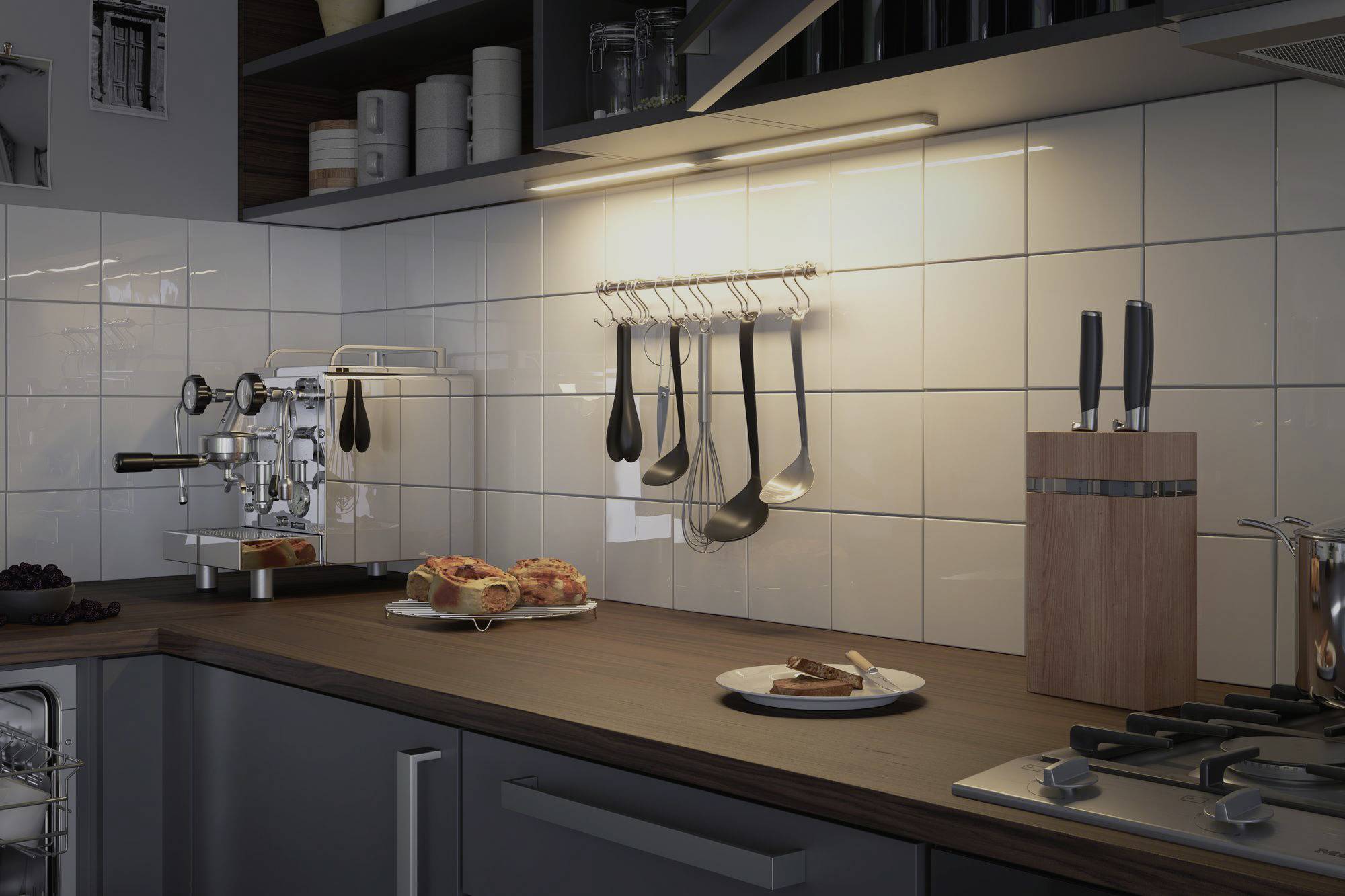 A modern kitchen with tiled walls. On the worktop are a coffee machine, cake, crockery, knife block and kitchen utensils.