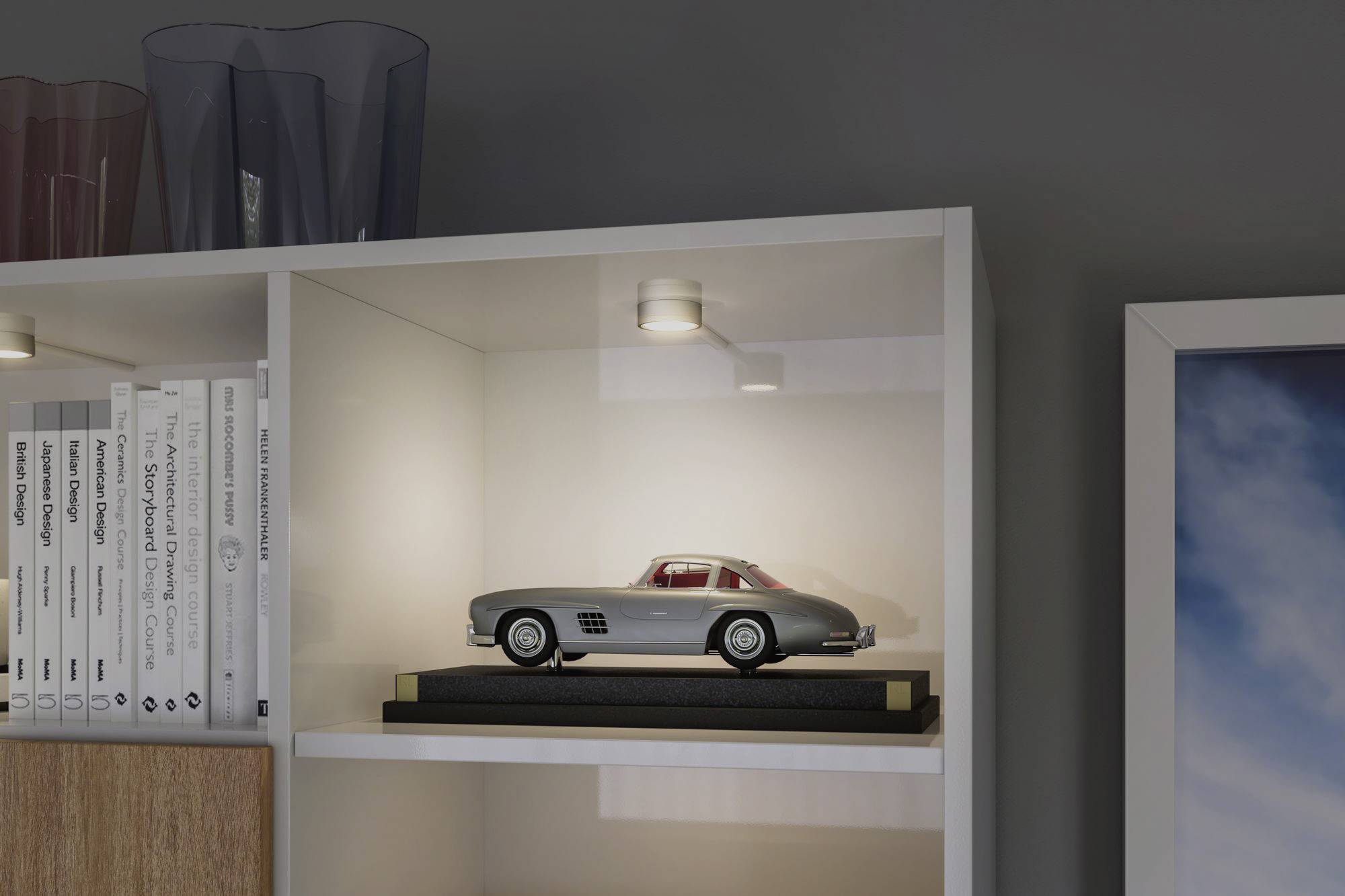 Toy car on the shelf, surrounded by books and pictures.