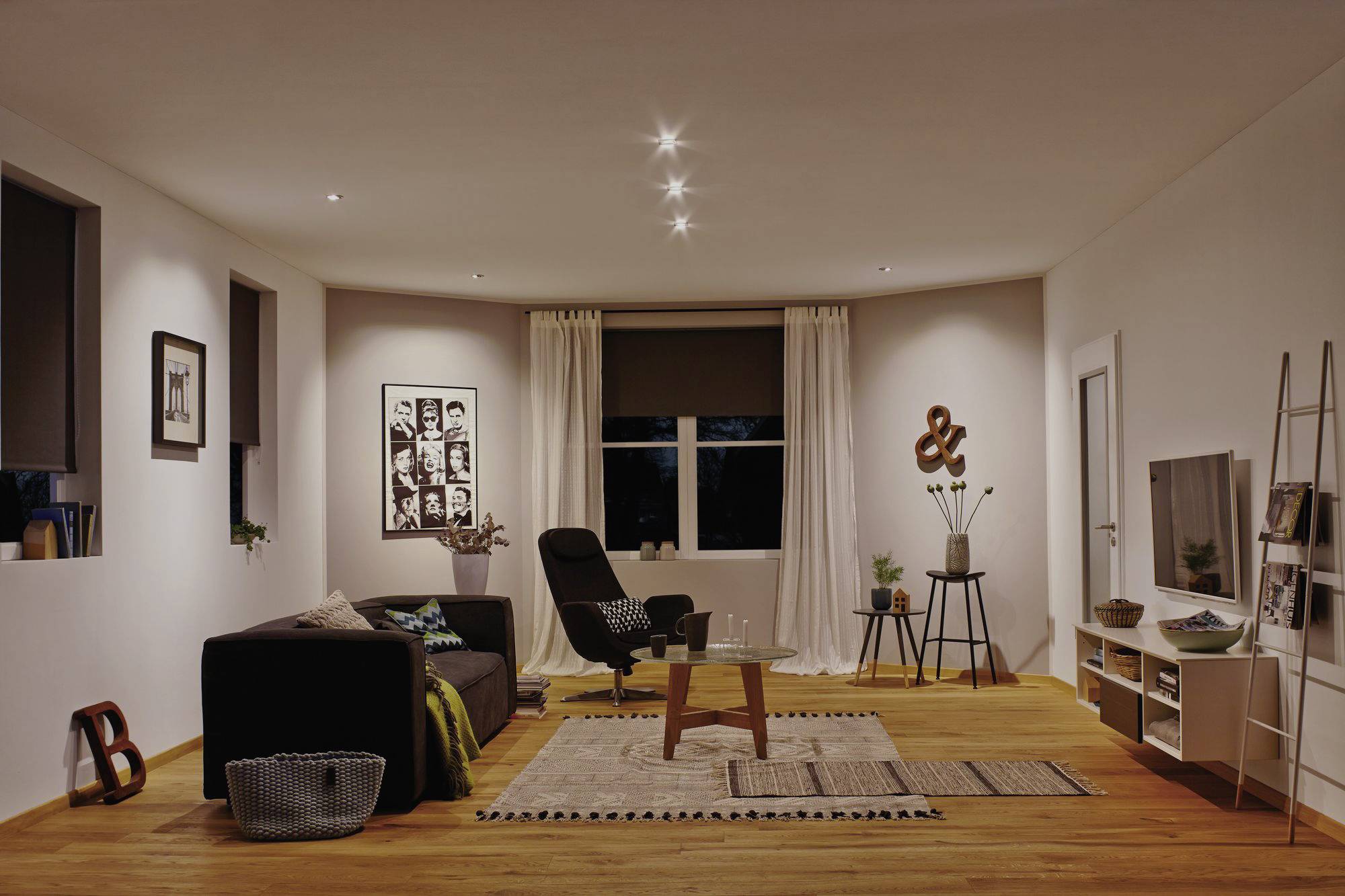 A modern furnished living room with a sofa, rug, armchair, coffee table and shelving. Subtle lighting and wall decoration.