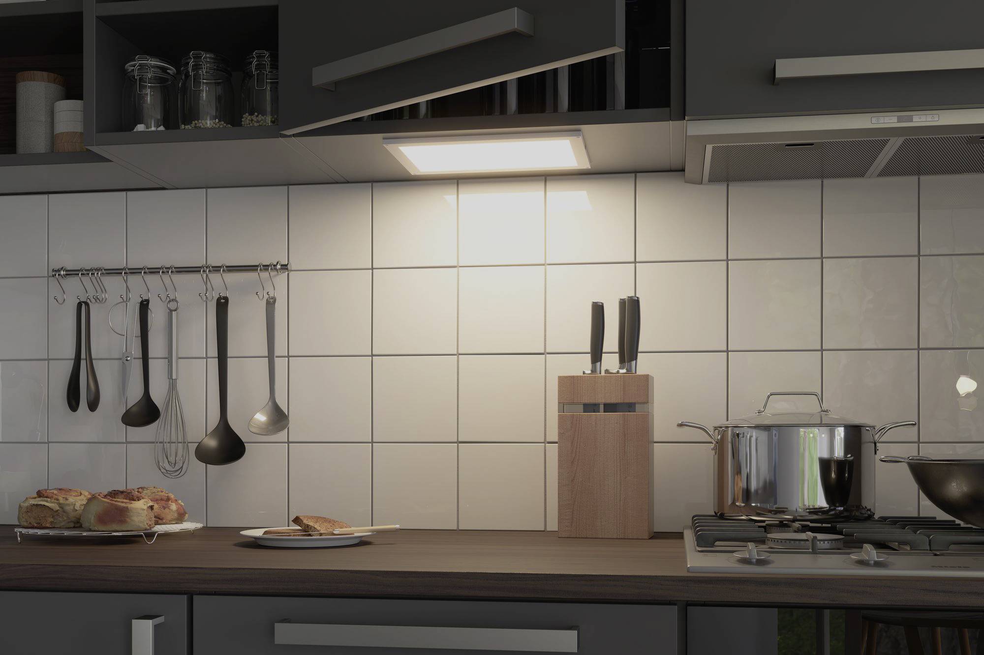 Kitchen with tiled splashback, modern cupboards, hanging utensils, bread plate, knife block and soup pot on the hob.