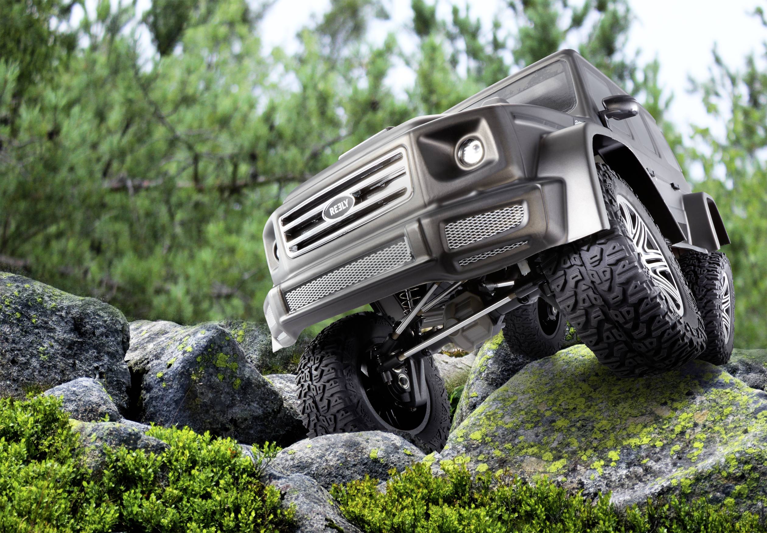 A 4x4 drives over rocky terrain, surrounded by green foliage. Front view reveals robust tyres and vehicle front.