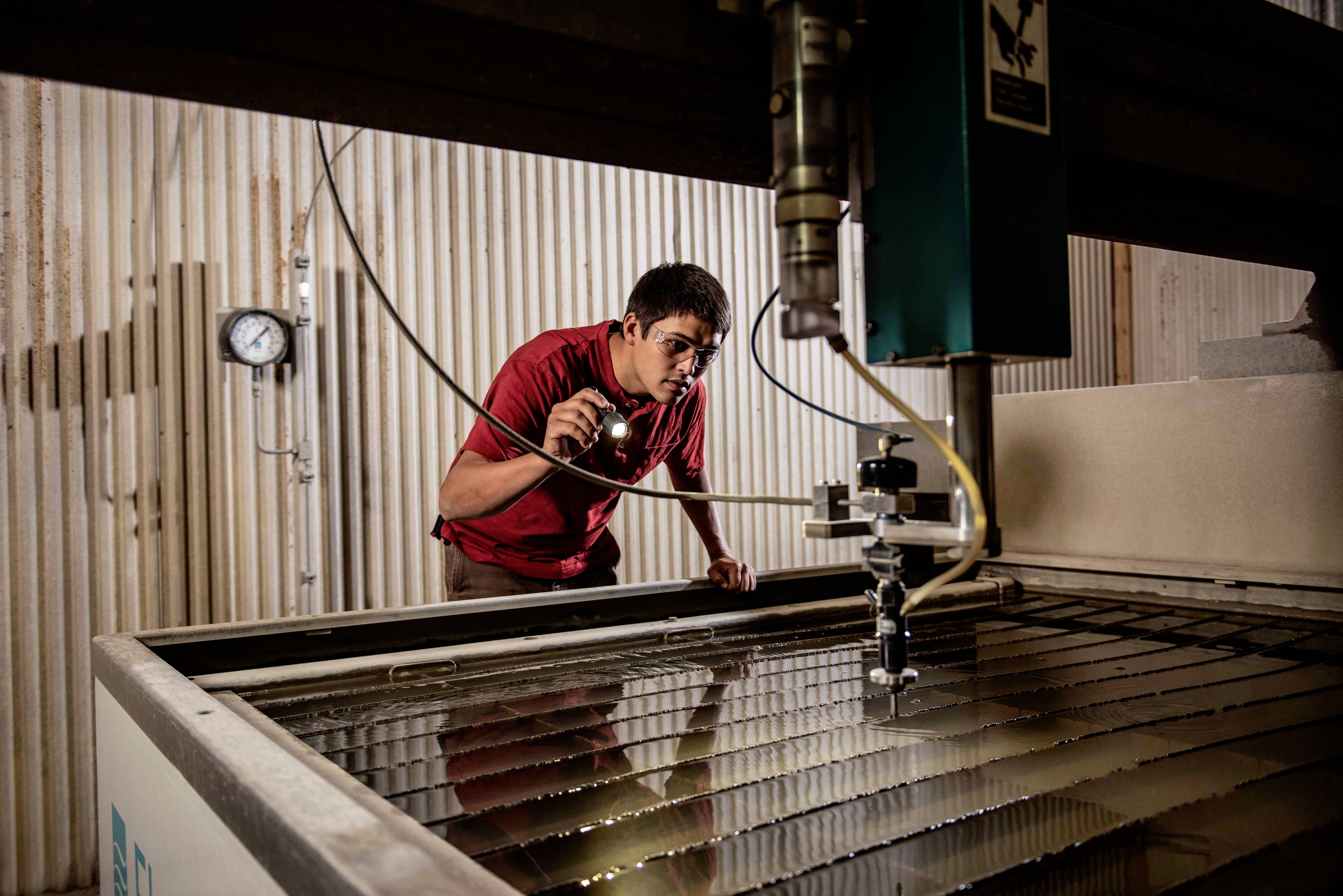 A technician with a torch inspects an industrial machine in a factory environment to identify potential issues.