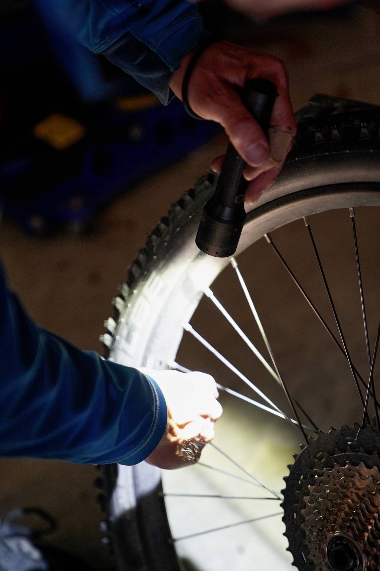 A person is inspecting the bicycle's rear wheel with a torch in the dark. Focus is on the spokes and the chain.