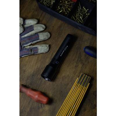 A torch lies on a wooden table, surrounded by screws in a container, a work glove, and tools.