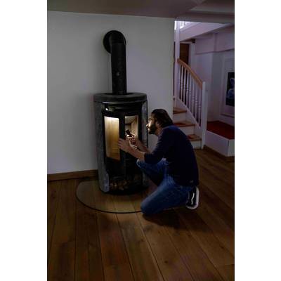 A person is sitting on the floor and lighting a fire in a modern fireplace in a cosy room with a wooden floor.