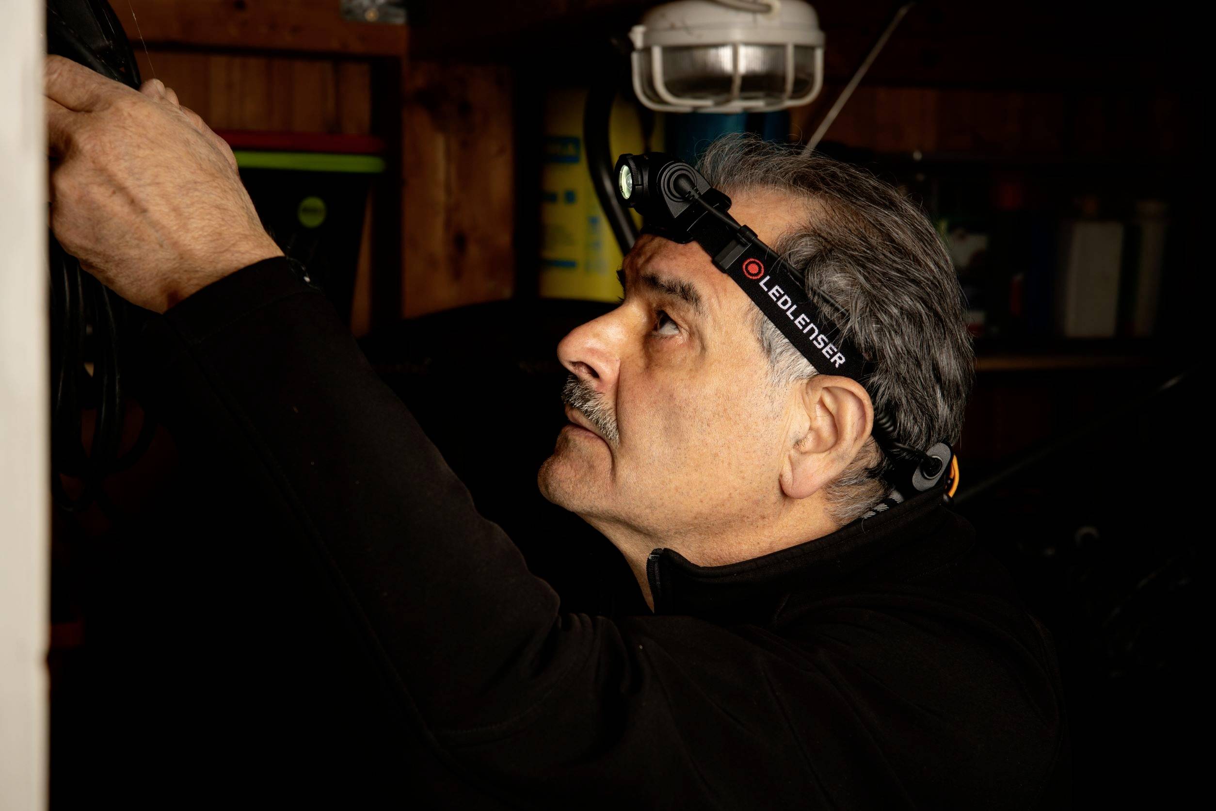 A man is wearing a head torch and working on something outside the frame. He is in a dimly lit room.