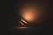 A modern table lamp radiating against a dark background lighting creates a warm, orange light in a dim room.