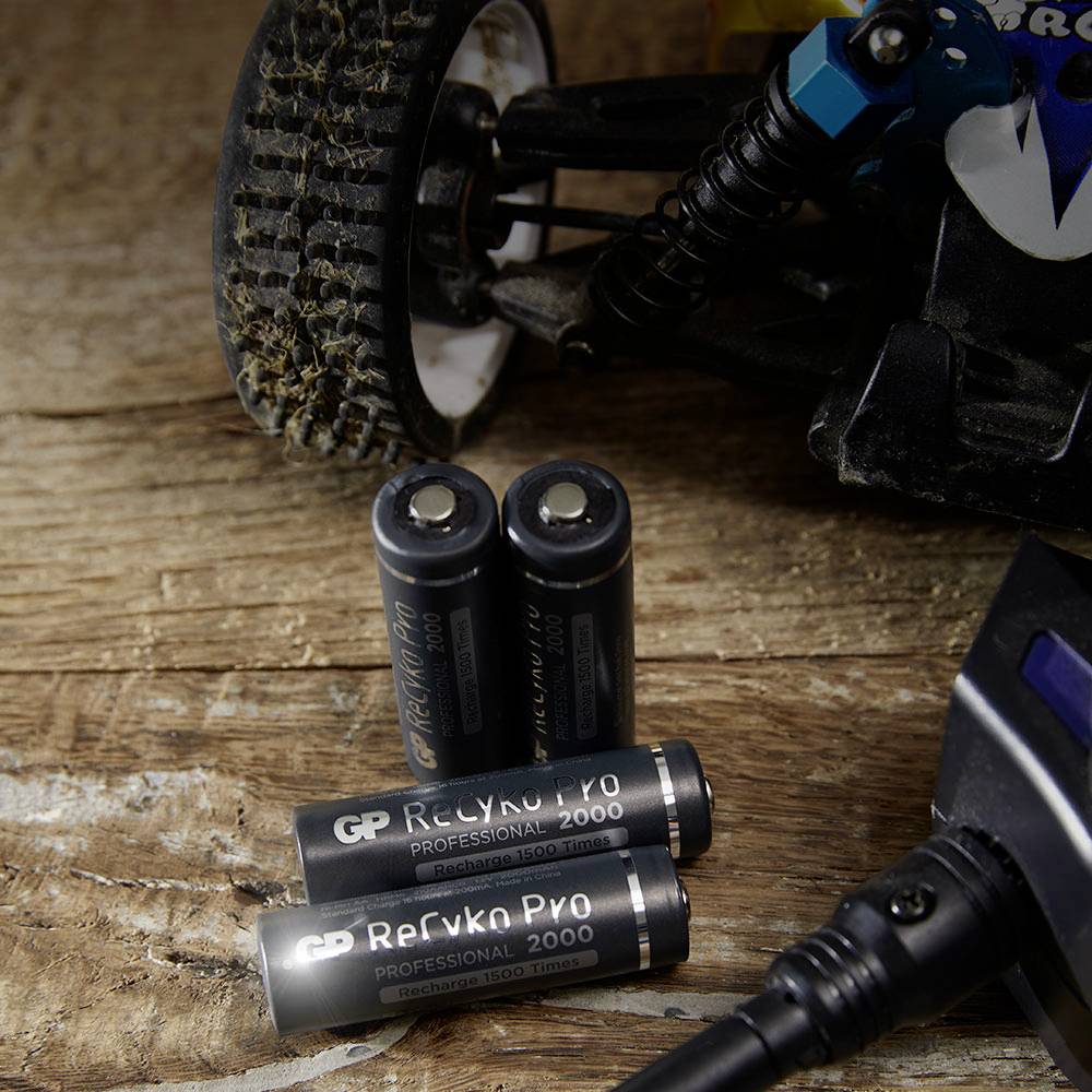 The image shows two AA batteries lying on a wooden table, next to a model car that is being charged.