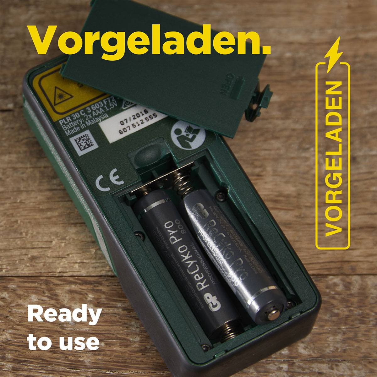 A battery compartment with two AA batteries, which are labelled as 'pre-charged' and 'ready to use', is lying on a wooden table.