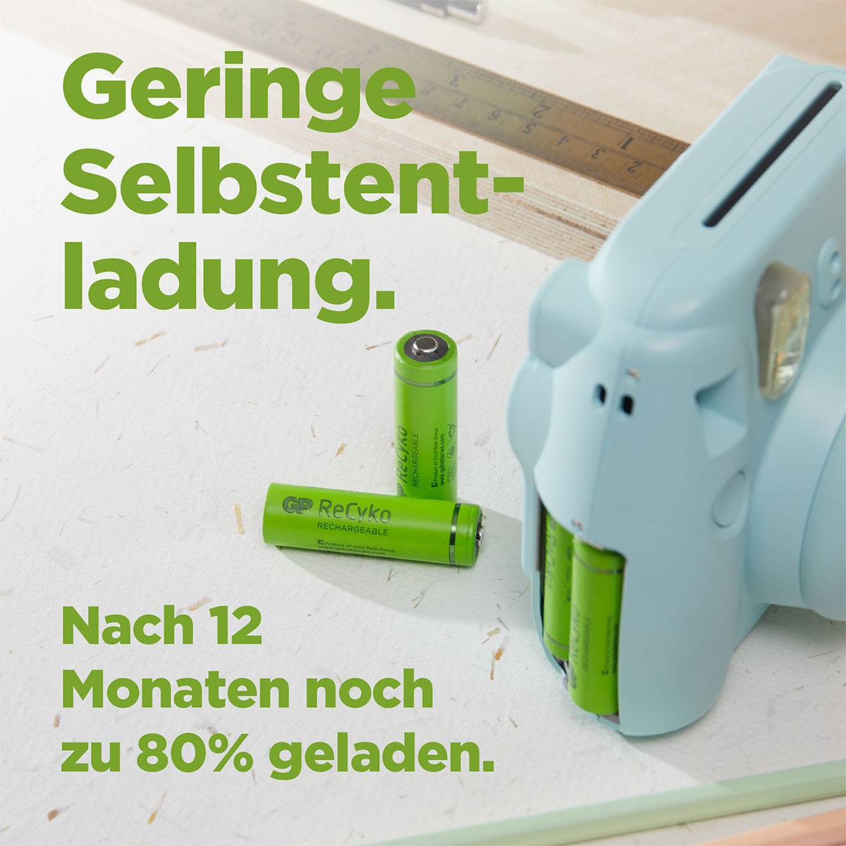 Green rechargeable battery with charger on wooden table. Text: 'Low self-discharge. Still 80% charged after 12 months.'