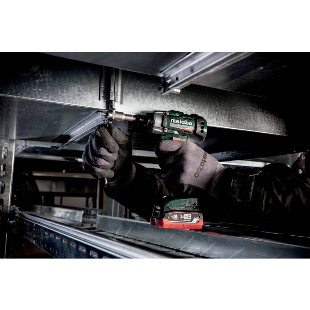A person wearing gloves uses a Metabo power tool to tighten a bolt on a metal structure in an industrial setting.