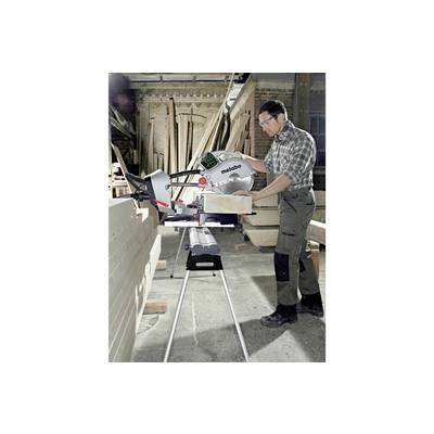 A man is operating a circular saw in a workshop, sawing a long wooden board. Timber stacks in the background. Wearing appropriate safety protection.